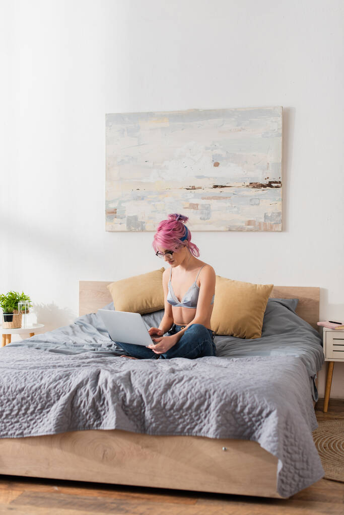 giovane freelance con capelli tinti utilizzando il computer portatile in camera da letto - Foto, immagini