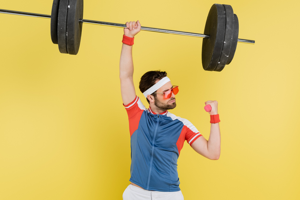 Sportsman lifting barbell and dumbbell isolated on yellow  - Photo, Image