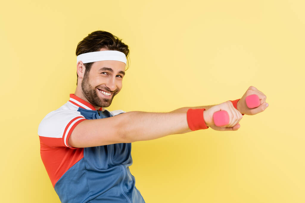Positives Sportler-Training mit Kurzhanteln und Blick auf Kamera isoliert auf gelb  - Foto, Bild