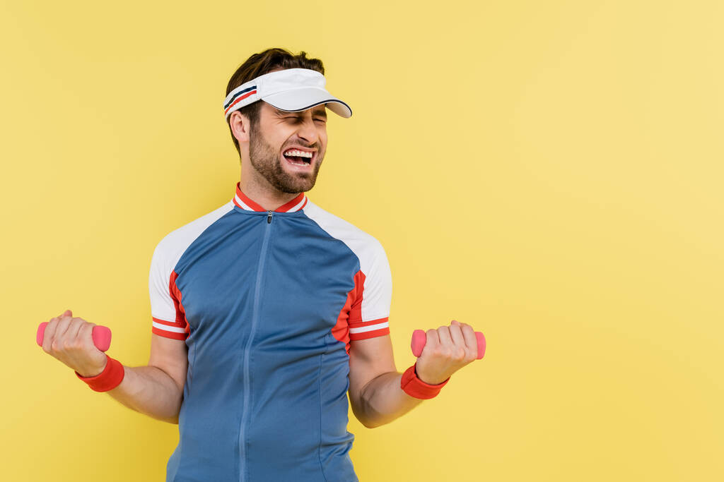 Sportsman in visor training with dumbbells isolated on yellow  - Photo, Image