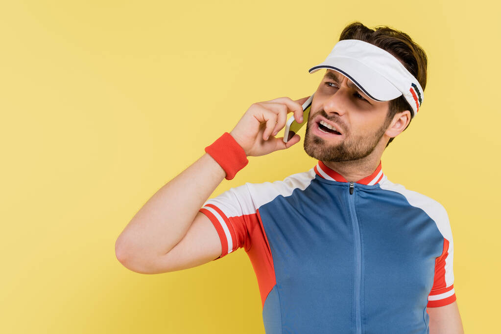 Zły sportowiec w visor mówi przez telefon komórkowy odizolowany na żółto  - Zdjęcie, obraz