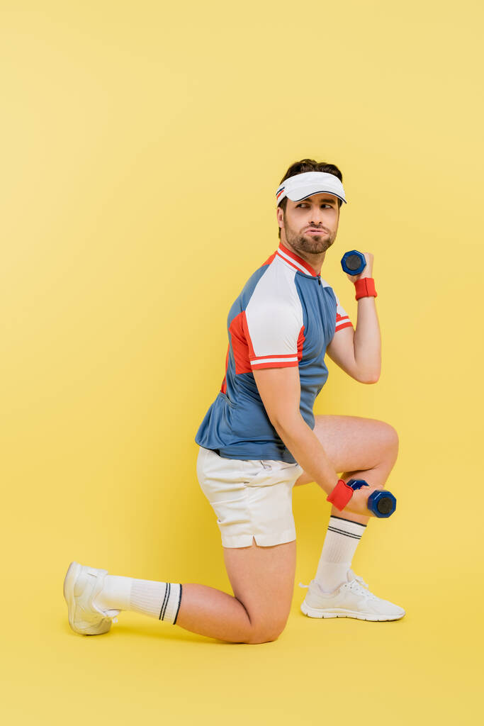 Bearded sportsman training with dumbbells and looking away on yellow background  - Photo, Image