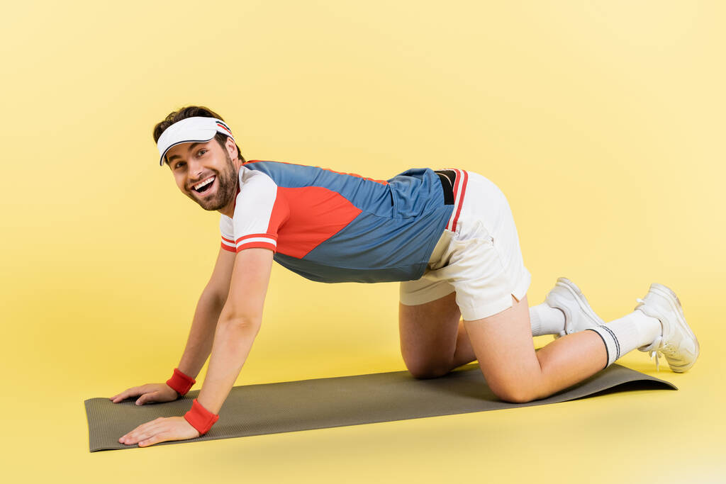 Позитивный спортсмен стоит на коврике для фитнеса на желтом фоне  - Фото, изображение