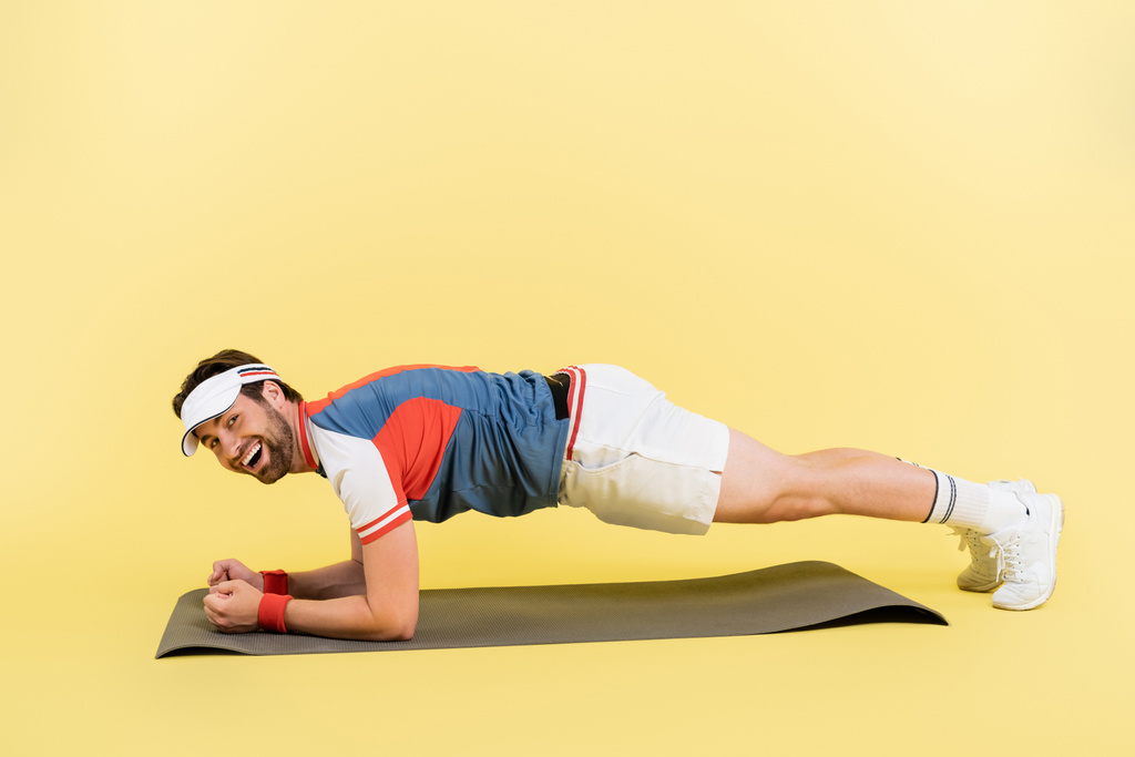 Positieve sporter staat in plank op fitness mat op gele achtergrond  - Foto, afbeelding