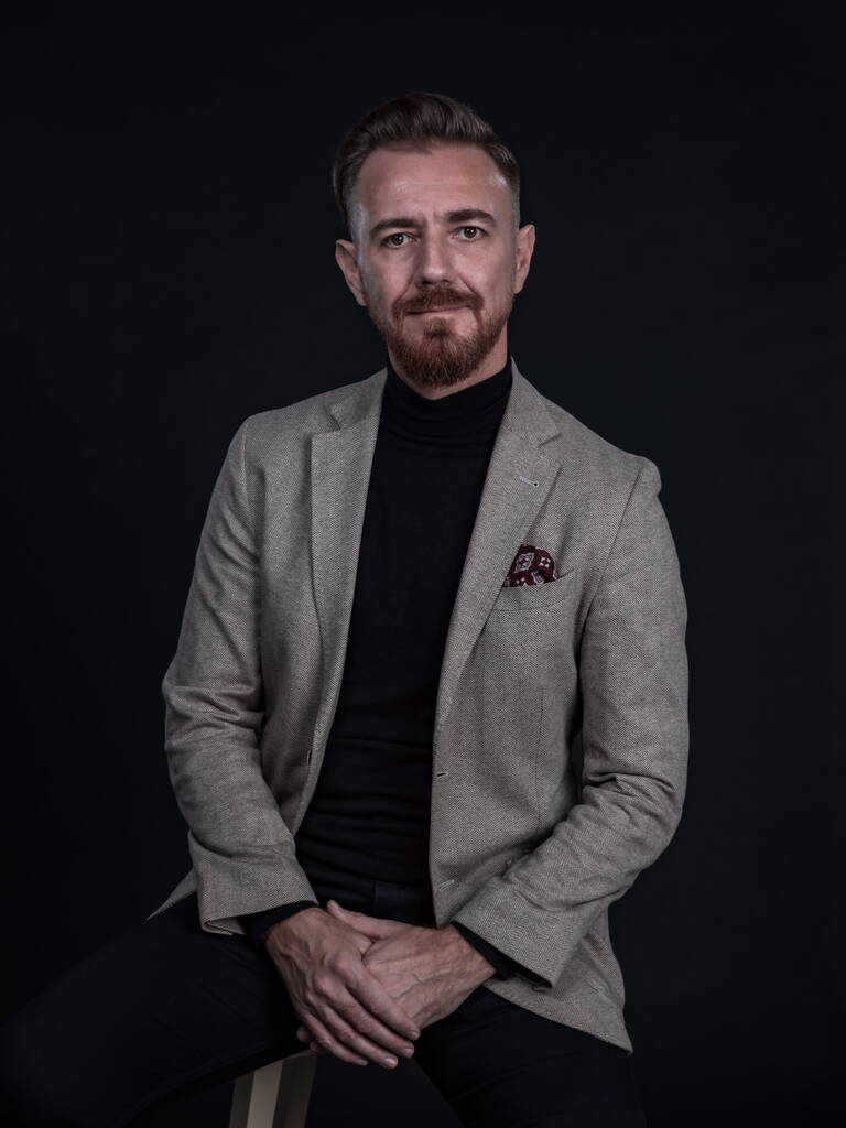 Portrait d'un homme d'affaires adulte vêtu d'un costume tendance et assis dans un studio moderne sur une chaise élégante sur fond noir - Photo, image