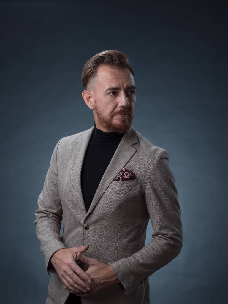 Retrato de un elegante y elegante hombre de negocios con barba y ropa de negocios casual en un estudio fotográfico aislado sobre un fondo oscuro con las manos - Foto, imagen