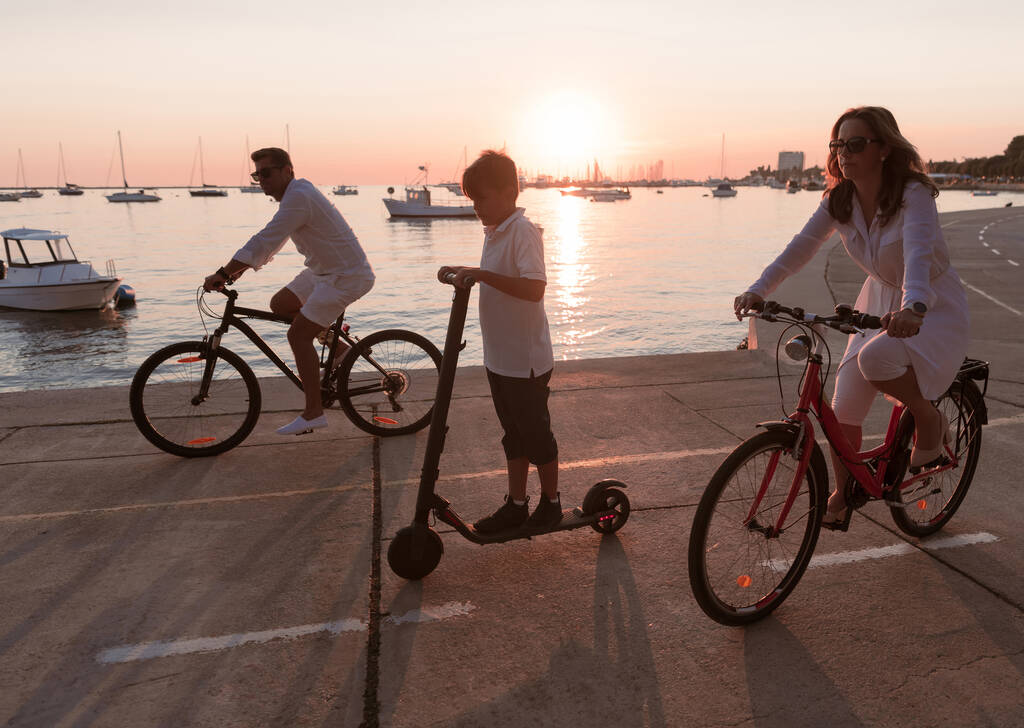 Familia feliz disfrutando de una hermosa mañana junto al mar juntos, los padres montando una bicicleta y su hijo montando un scooter eléctrico. Enfoque selectivo  - Foto, Imagen