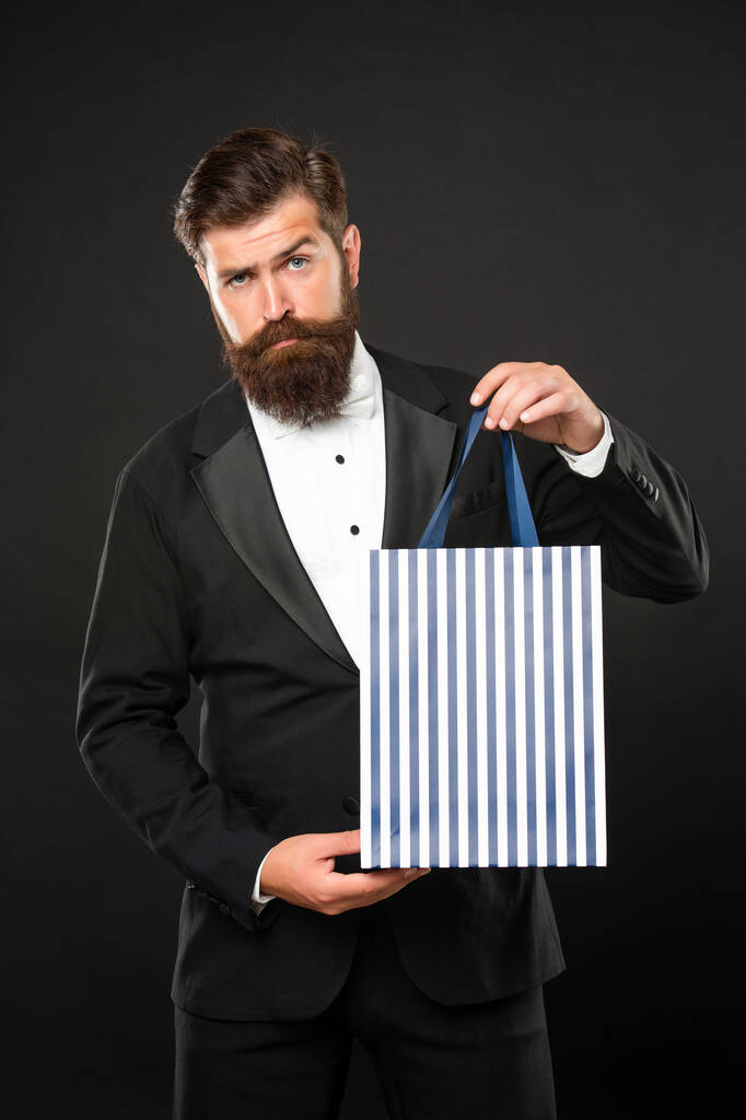 hombre en esmoquin corbata de lazo sobre fondo negro presentando bolsa de compras. San Valentín. espacio de copia. - Foto, Imagen