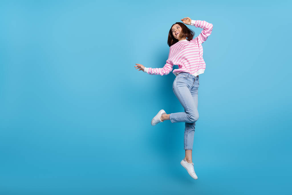 Foto de mujer dulce niña usar suéter a rayas saltando alto buscando espacio vacío aislado color azul fondo - Foto, imagen