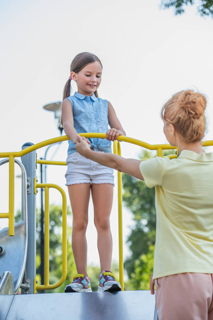mulher segurando a mão da filha de pé no slide no parque de diversões - Foto, Imagem
