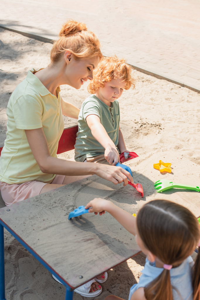 Lächelnde Frau und Kinder, die draußen mit Harken und Sand spielen - Foto, Bild