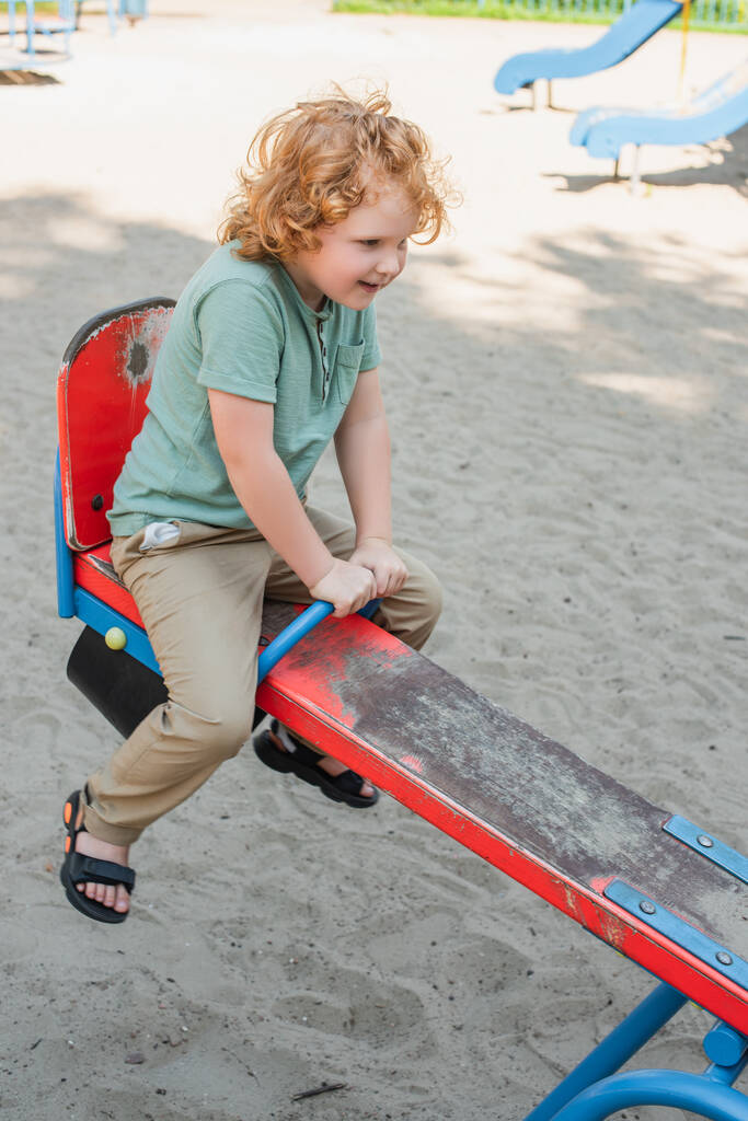 volle Länge Ansicht der glücklich Rotschopf Junge Reiten Wippe in Freizeitpark - Foto, Bild