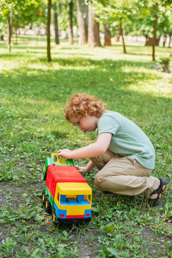 άποψη πλήρους μήκους του αγοριού που παίζει με φορτηγό παιχνίδι στο πράσινο γρασίδι - Φωτογραφία, εικόνα
