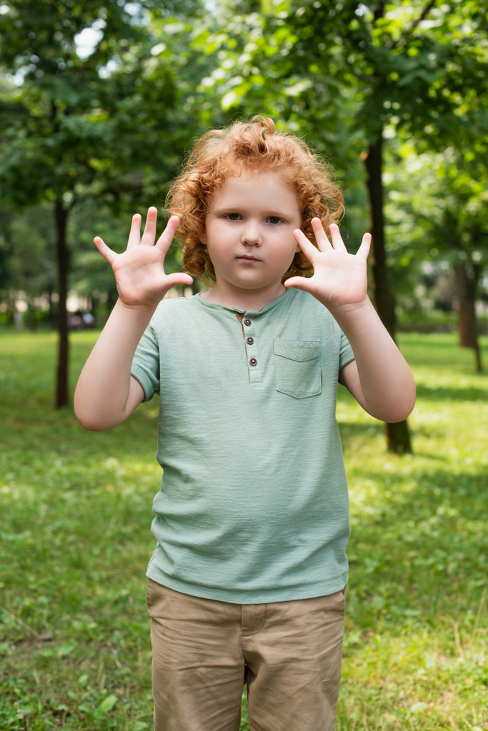 niño en camiseta mostrando las palmas limpias mientras mira la cámara al aire libre - Foto, Imagen