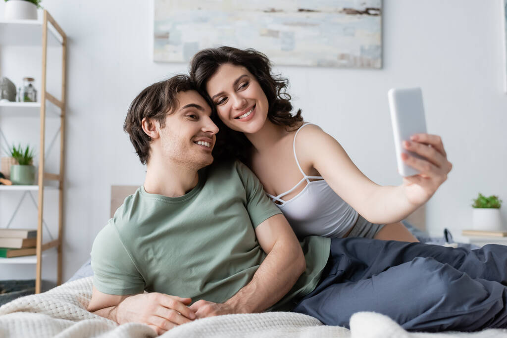 Mutlu ve genç bir çift yatak odasında selfie çekiyor. - Fotoğraf, Görsel