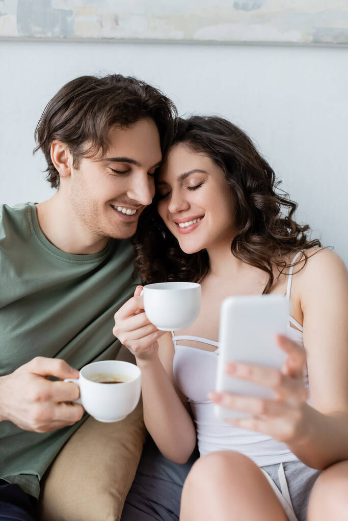 felice giovane coppia con gli occhi chiusi in possesso di tazze e prendendo selfie - Foto, immagini