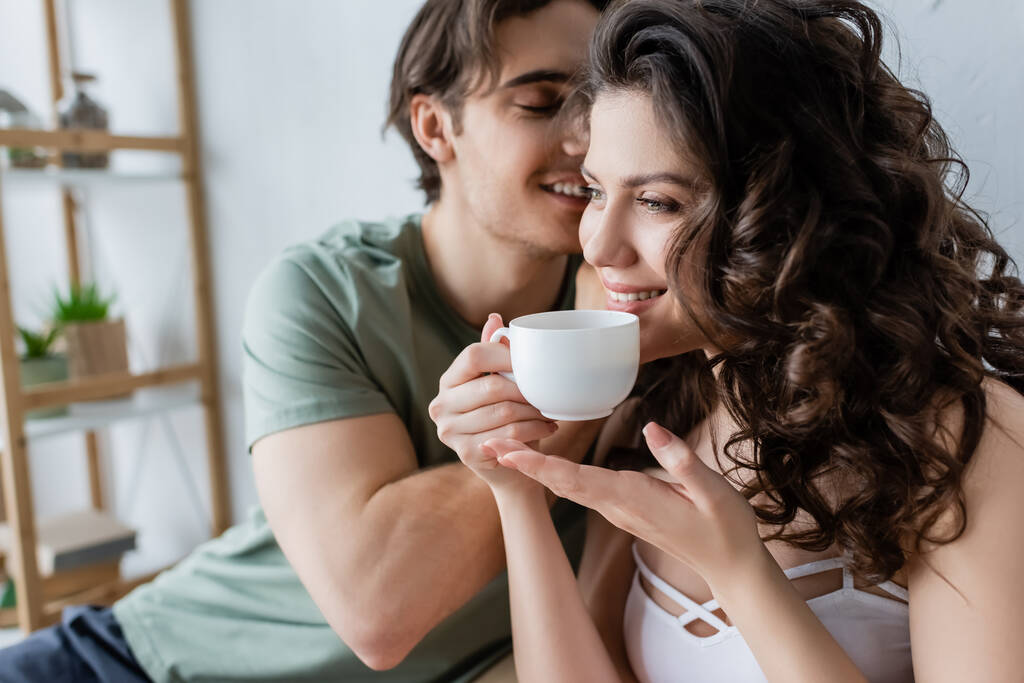 fröhlicher Mann küsst glückliche Freundin mit Tasse Kaffee - Foto, Bild