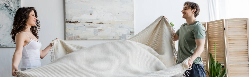 вид сбоку улыбающейся молодой пары, держащей одеяло, баннер - Фото, изображение
