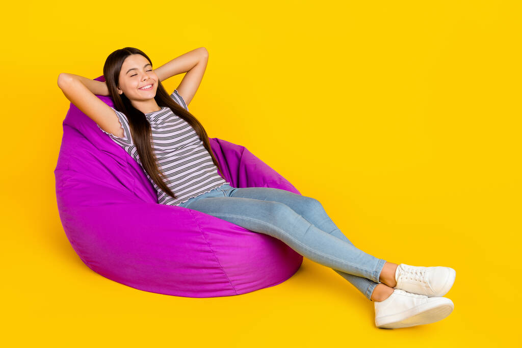 Foto lateral de perfil de tamaño completo de las manos de ensueño niña detrás de la cabeza relajarse silla violeta suave aislado sobre fondo de color amarillo - Foto, Imagen