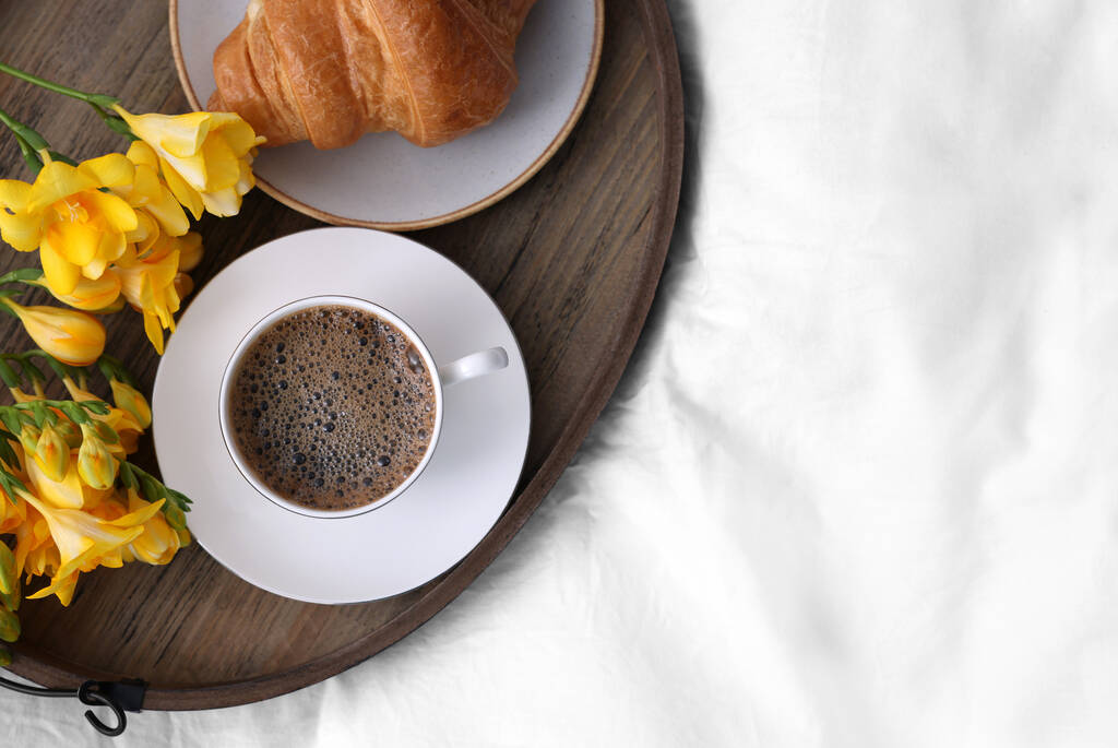 Ochtendkoffie, croissant en bloemen op bed, bovenaanzicht. Ruimte voor tekst - Foto, afbeelding