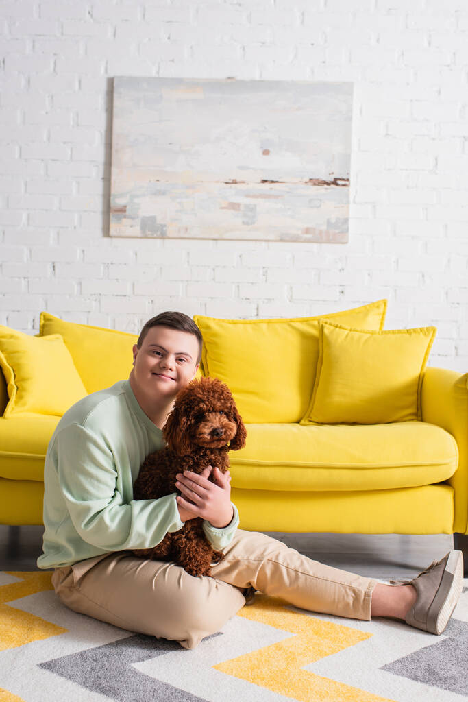 Щасливий хлопчик-підліток з синдромом Дауна обіймає пудель у вітальні
  - Фото, зображення