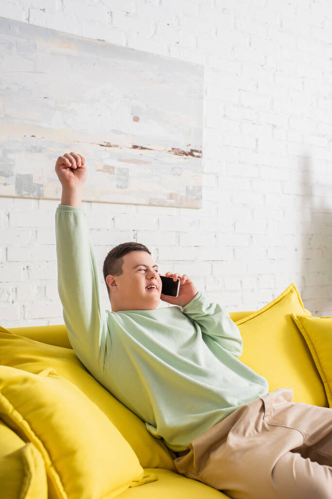 Adolescent excité avec le syndrome du duvet parlant sur smartphone sur le canapé à la maison  - Photo, image