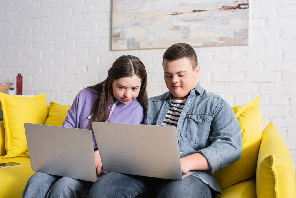 Jugendliche mit Down-Syndrom nutzen Laptop auf der heimischen Couch  - Foto, Bild
