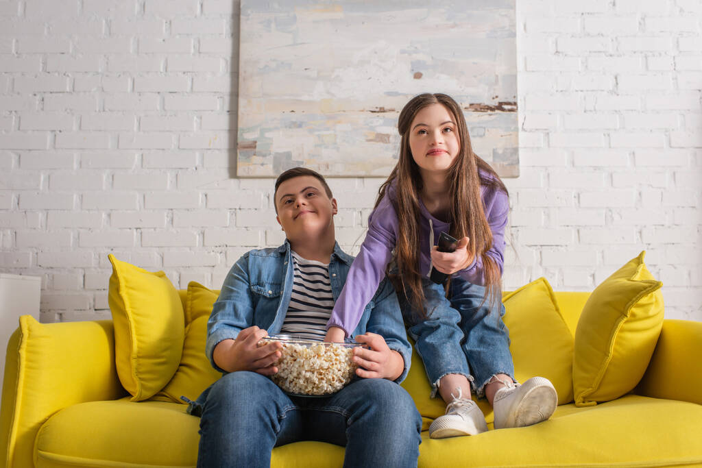 Έφηβοι με σύνδρομο down κρατώντας ποπ κορν ενώ βλέπουν τηλεόραση στο σπίτι  - Φωτογραφία, εικόνα