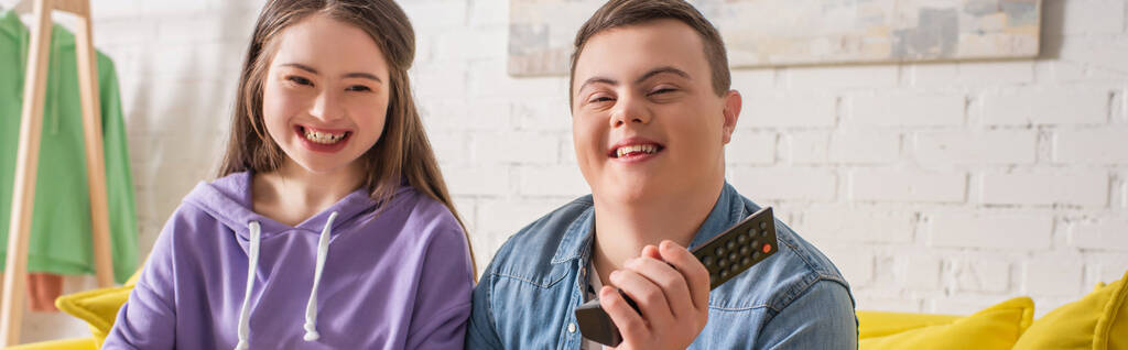 Adolescentes positivos con síndrome de Down sosteniendo mando a distancia en casa, pancarta  - Foto, imagen