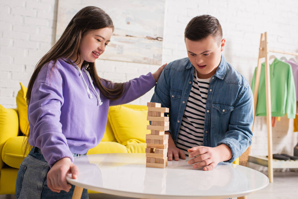 Позитивные друзья с синдромом Дауна играют в деревянные блоки игры на кофейном столике дома  - Фото, изображение