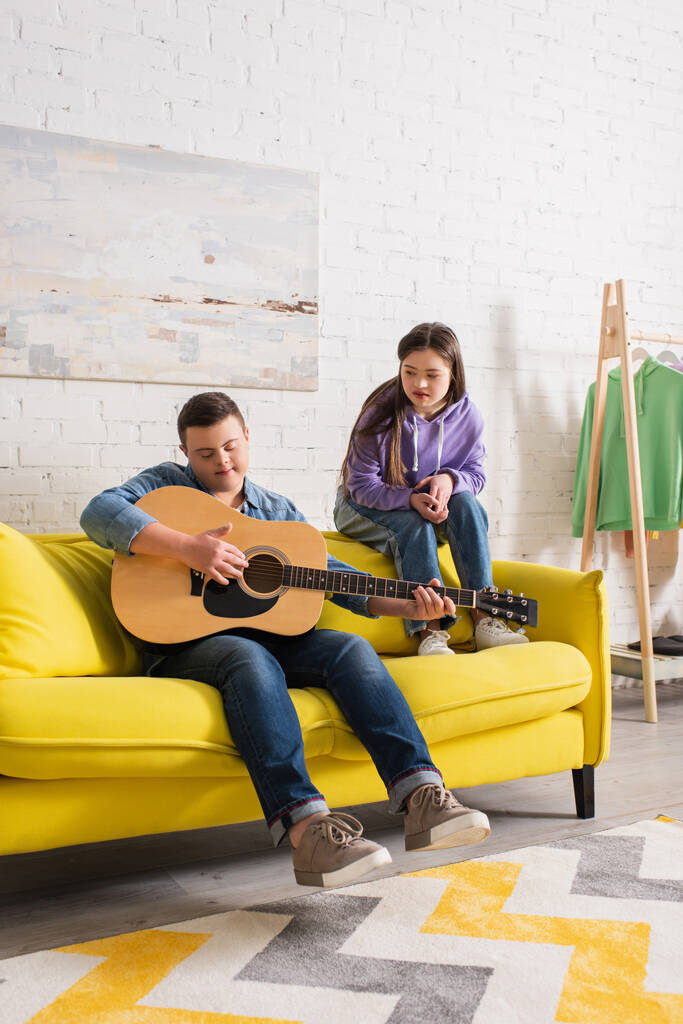 Подросток с синдромом Дауна играет на акустической гитаре рядом с другом дома  - Фото, изображение