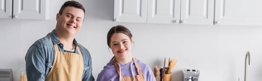Adolescentes sorridentes com síndrome de down olhando para a câmera na cozinha, banner  - Foto, Imagem