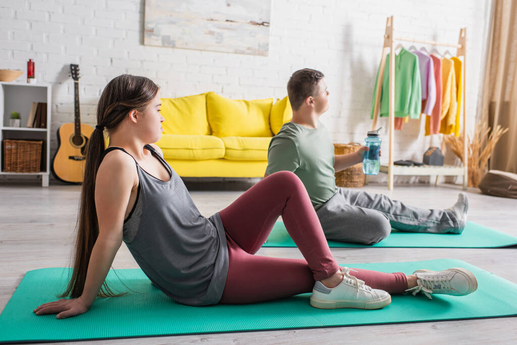 Oldalnézet tinédzser lefelé szindróma ül fitness mat közelében barátja otthon  - Fotó, kép