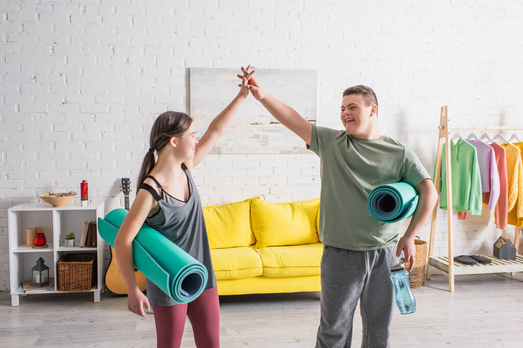 Adolescenti positivi con sindrome di Down che tengono tappeti fitness e danno il cinque a casa - Foto, immagini
