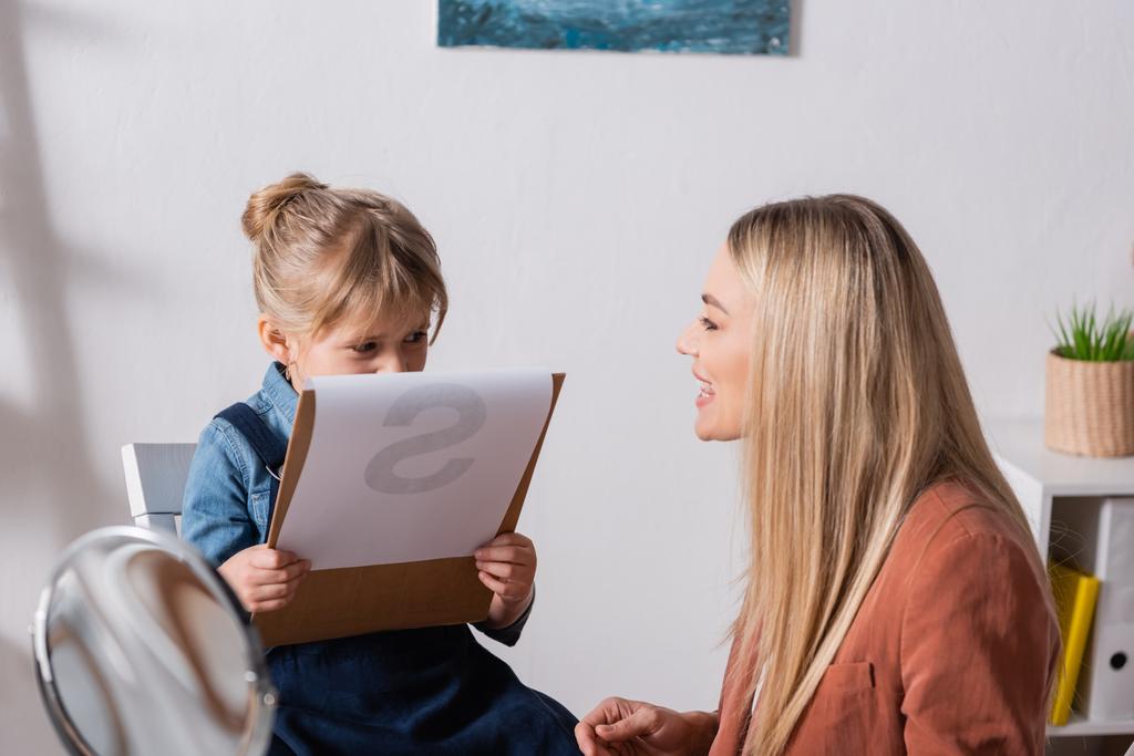 Orthophoniste parlant près d'un enfant tenant un presse-papiers en classe  - Photo, image