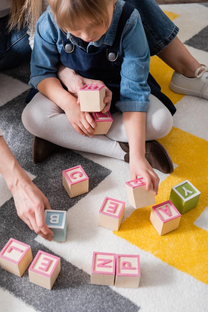 Girl holding wooden blocks with letters near speech therapist in consulting room  - Photo, Image