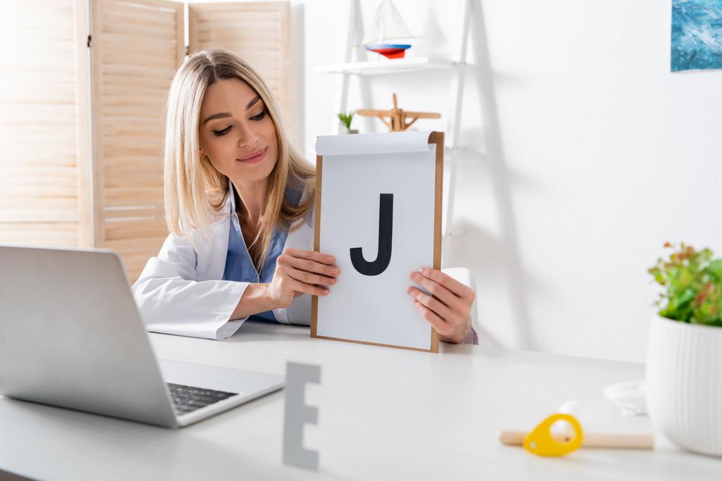 Speech therapist holding clipboard with letter during online lesson on laptop in consulting room  - Photo, Image