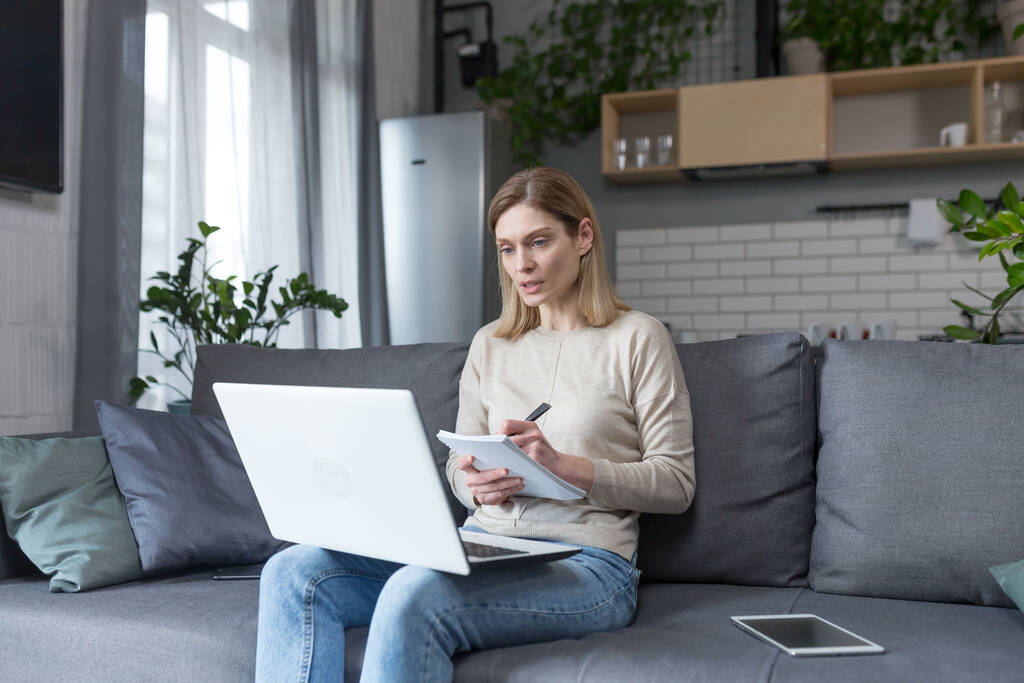 Donna a casa a studiare online utilizza il computer portatile seduto sul divano a casa - Foto, immagini