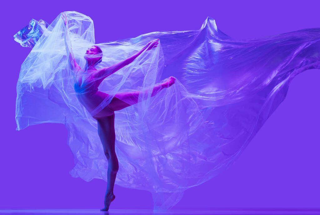 Portrét krásné ohebné ženy, baletka tančící s látkou na fialovém pozadí studia v neonu. Móda, styl, umění, krása - Fotografie, Obrázek