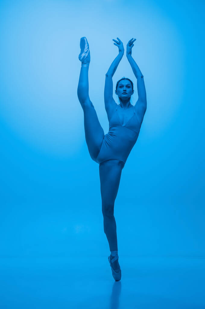 Grazia. Giovane e graziosa ballerina isolata su sfondo blu studio in luce al neon. Arte, flessibilità, concetto di ispirazione. - Foto, immagini