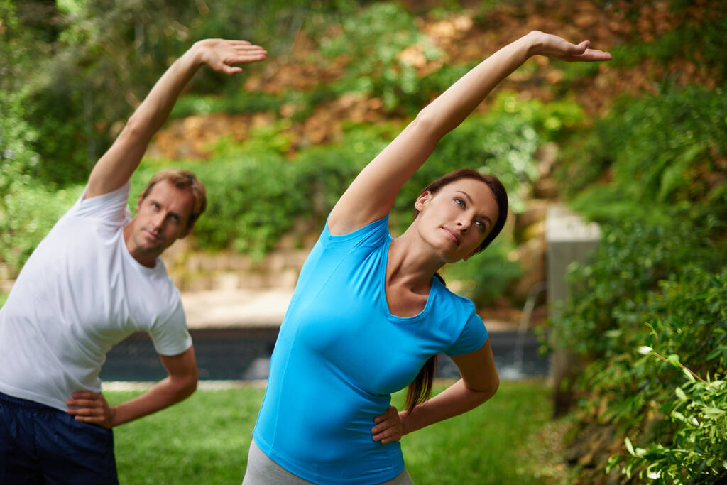 El camino hacia la flexibilidad. Fotografía de un hombre y una mujer realizando un estiramiento lateral en una clase de yoga al aire libre. - Foto, Imagen