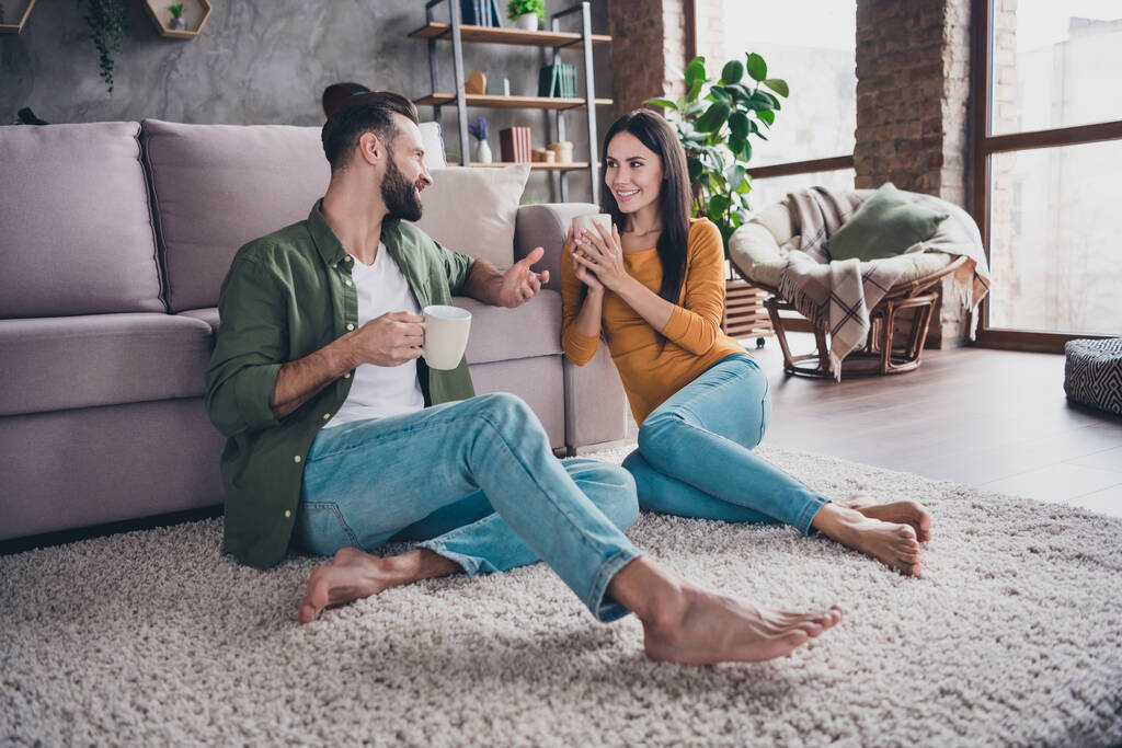 Portrait d'attrayant couple joyeux assis sur le tapis de sol communiquant passer la journée à boire du cacao à la maison appartement à l'intérieur - Photo, image