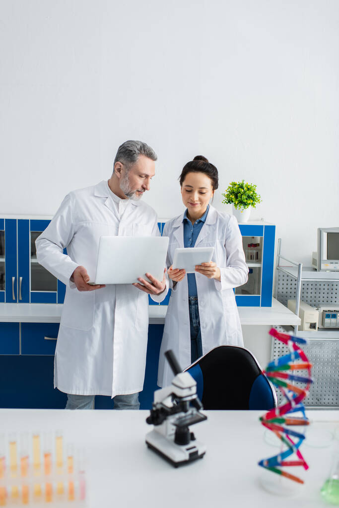 tutkijat valkoisissa takeissa seisoo kannettava tietokone ja digitaalinen tabletti laboratoriossa - Valokuva, kuva