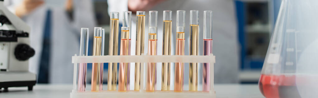Bulanık arkaplan ve pankartta, kırpılmış biyomühendislerin yakınındaki sıvıyla test tüplerinin seçici odağı - Fotoğraf, Görsel
