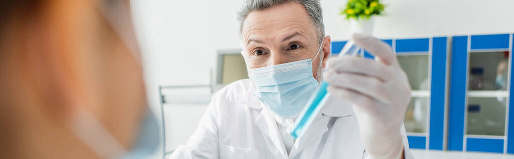 scientifique dans un masque médical tenant un tube à essai près d'un collègue flou, bannière - Photo, image