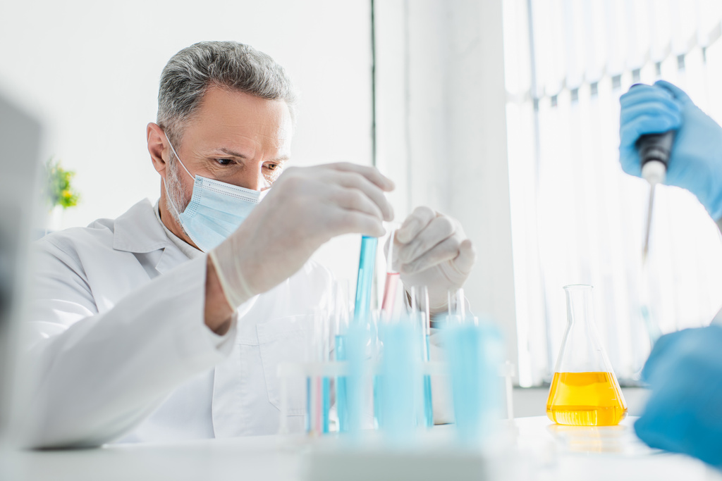 биоинженер в медицинской маске держит пробирки в лаборатории - Фото, изображение