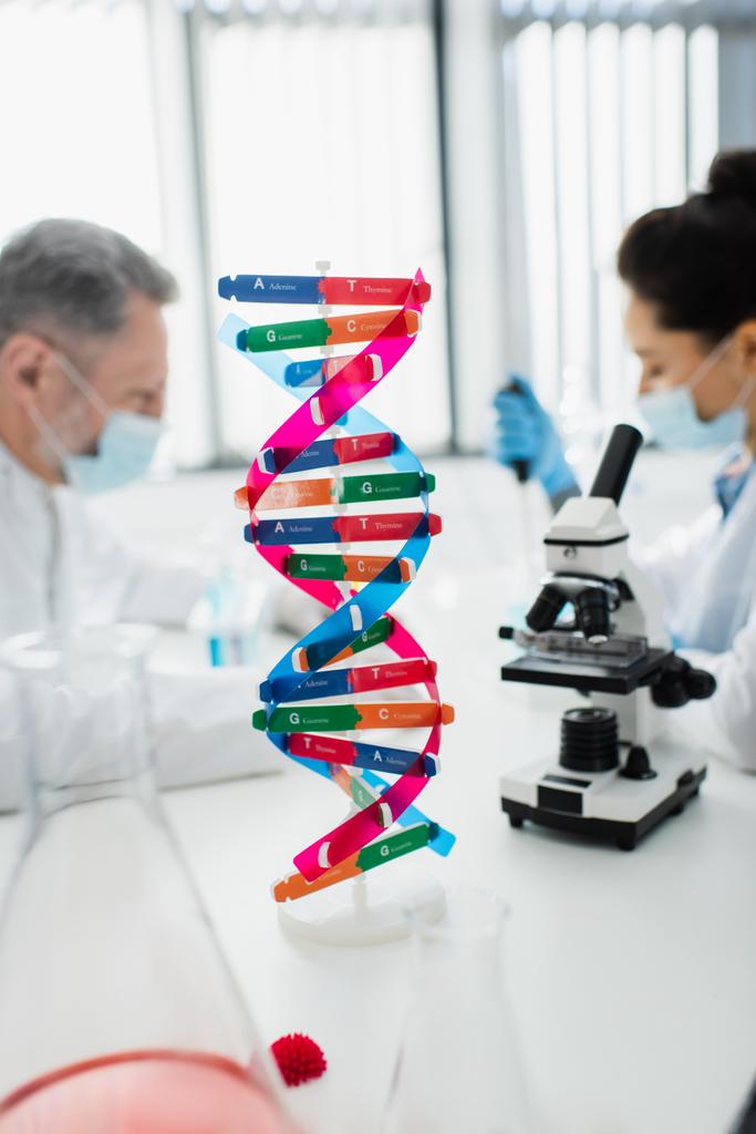 селективний фокус структури ДНК поблизу мікроскопа та генетиків у медичних масках на розмитому фоні
 - Фото, зображення