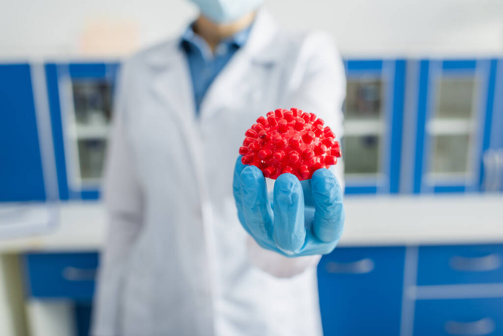 επιλεκτική εστίαση του κόκκινου μοντέλου βακτηρίων coronavirus στο χέρι του καλλιεργημένου επιστήμονα σε θολή φόντο - Φωτογραφία, εικόνα