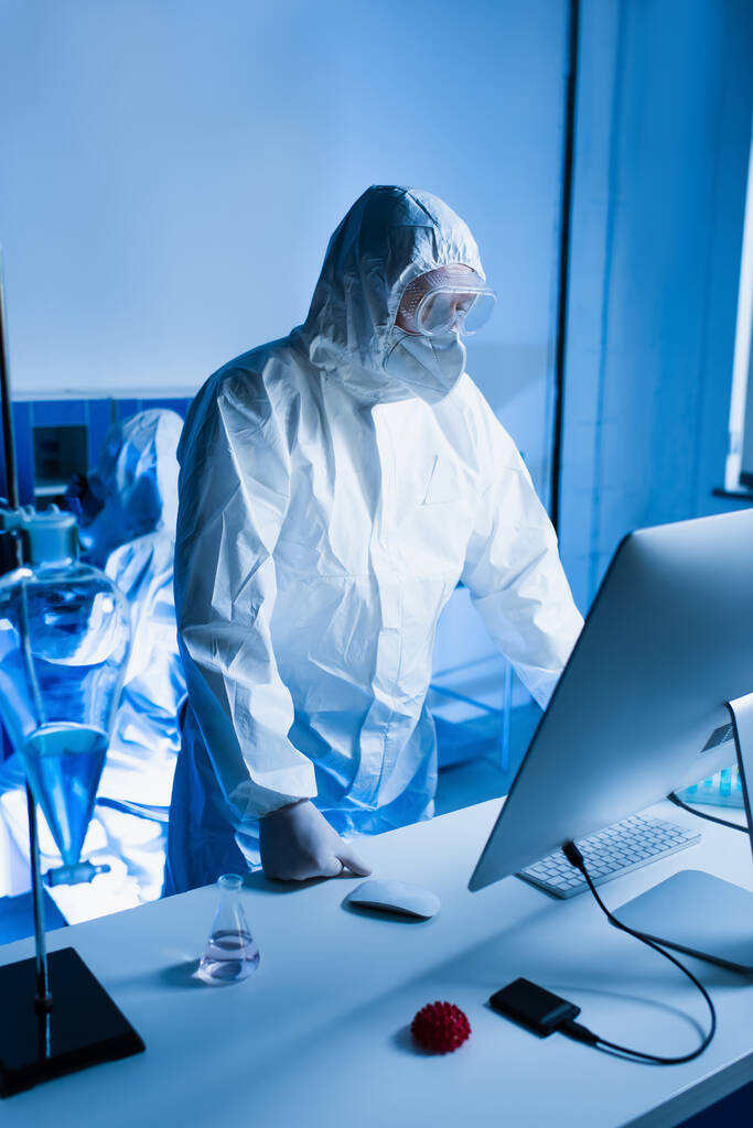 scientifique en combinaison Hazmat debout près de moniteur d'ordinateur en laboratoire - Photo, image