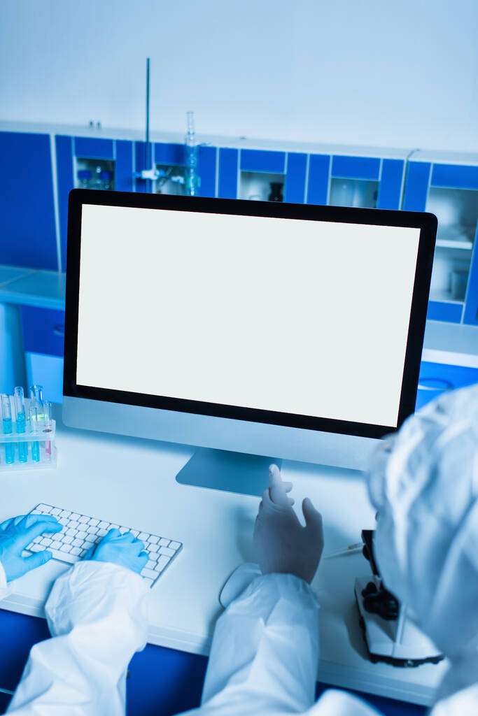 visão recortada do cientista em luvas de látex apontando para monitor com tela branca enquanto colega digitando no teclado - Foto, Imagem